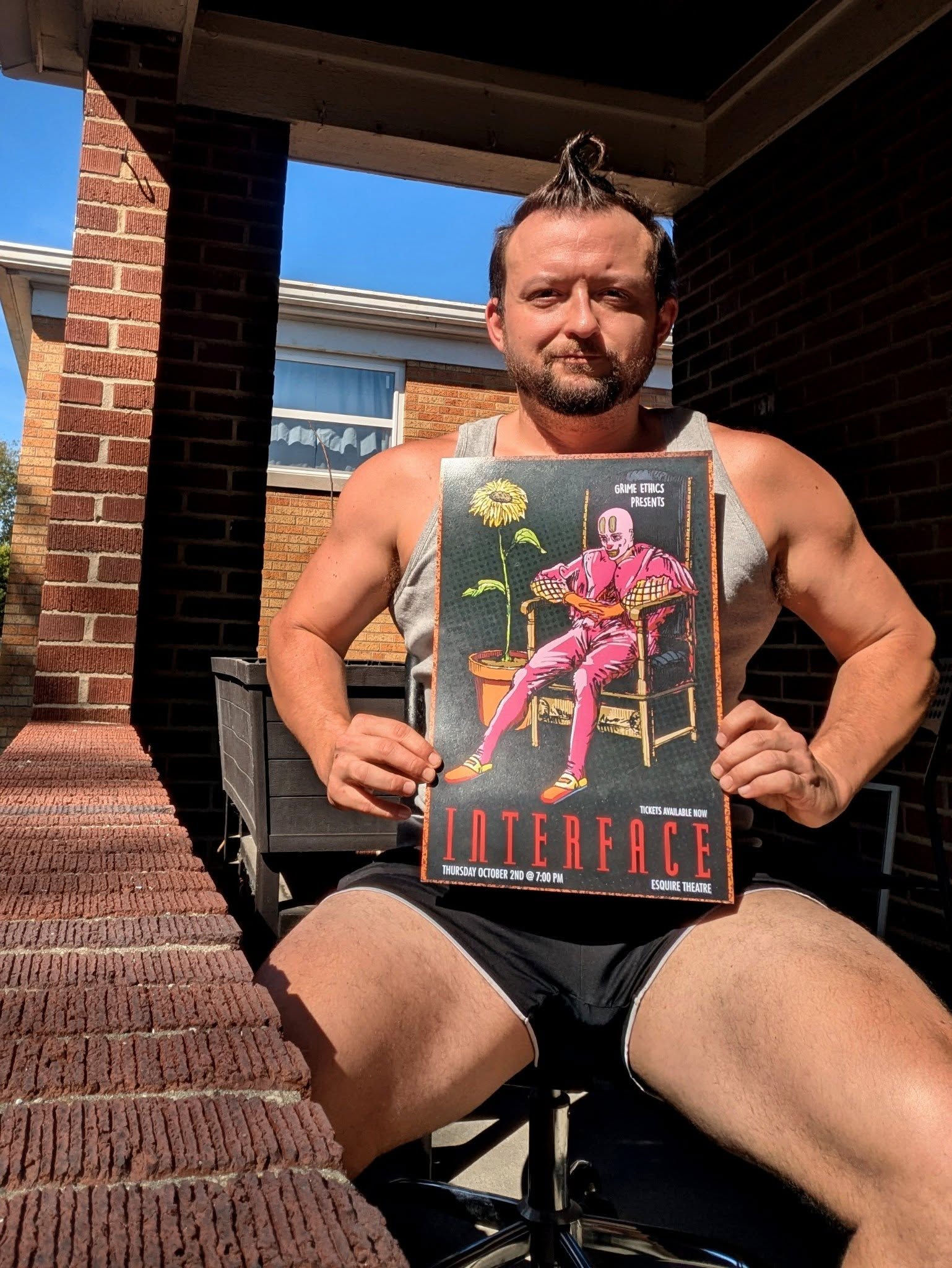 Justin Sovine holding the pink-chair Interface poster on a brick porch in the sun